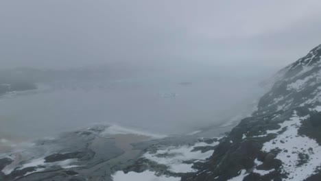 Drone-Shot-of-Man-on-Lookout-Above-Frozen-Glacial-Lake-and-Glacier-in-Landscape-of-Iceland,-50fps