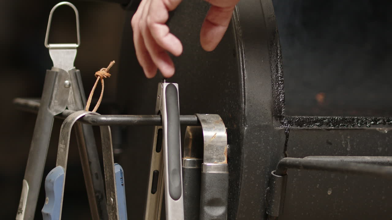 la tapa del pozo de barbacoa se abre y el humo sale mientras el hombre agarra las pinzas.