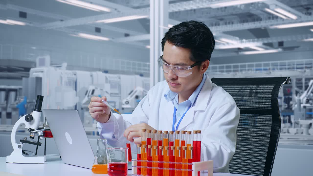 아시아 남성 과학자가 시험관으로 실험을 하고 현미경으로 실험실에서 노트북으로 타이핑을 하는 면적의 근접한 도 뷰.