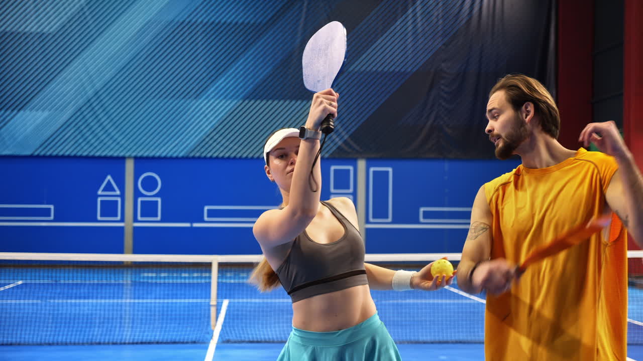 A man teaching a woman how to play pickleball in an inside court