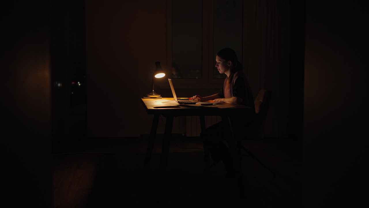 una mujer por la noche bajo una lámpara trabaja desde casa en la oscuridad. hora de la noche para el trabajo plazos son plazos de quema.