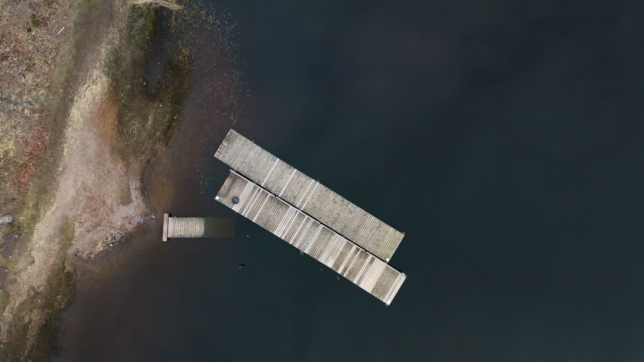 Floating high above a dock a drone lowers towards the dark waters framing the wooden structure in a slow spin.