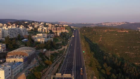 aerial view of a highway adjacent to an urban residential area and hills at sunrise