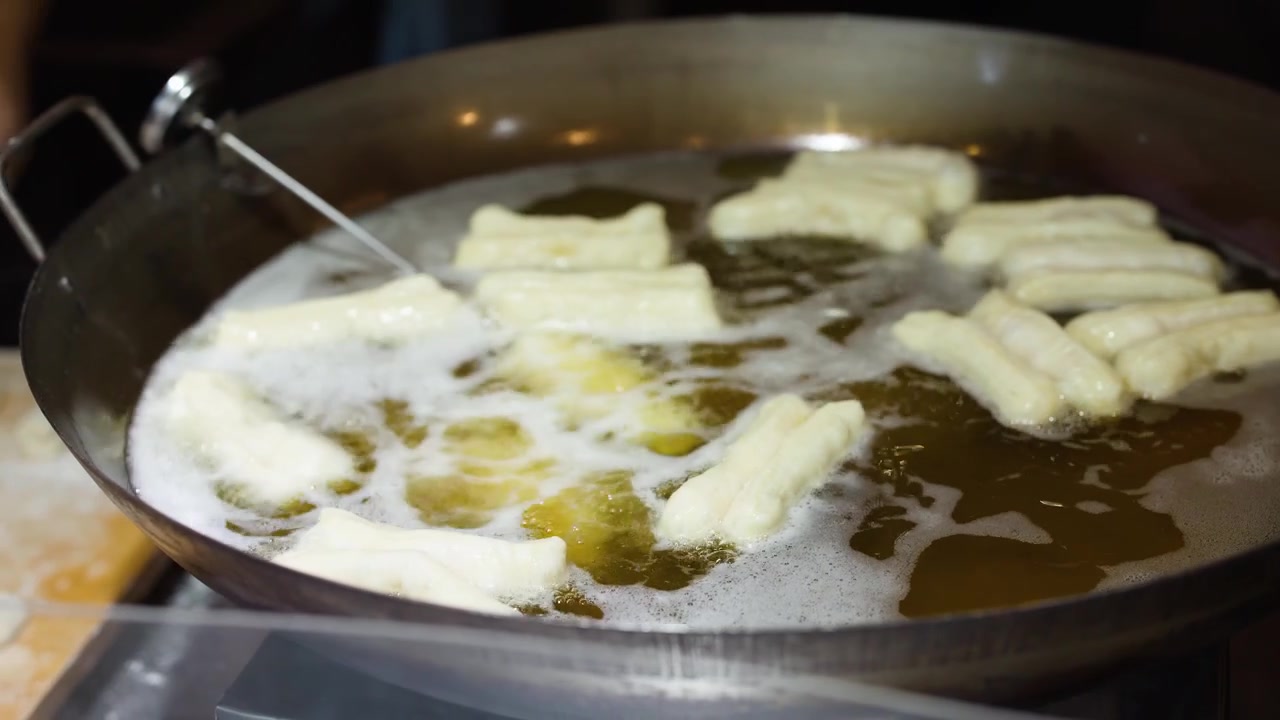 Close-up of a chef frying traditional Asian dough sticks in bubbling oil within a wok.