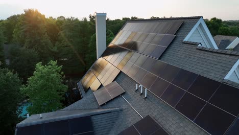 Solar panel Units on roof of American house in suburb during sunset time. Production of green energy. Aerial closeup. Reflection of sun on photovoltaic unit arrays. Modern neighborhoods