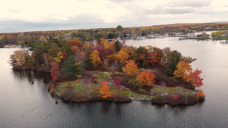 Stunning-aerial-view-of-island-in-a-lake-filled-with-colourful-trees-during-fall