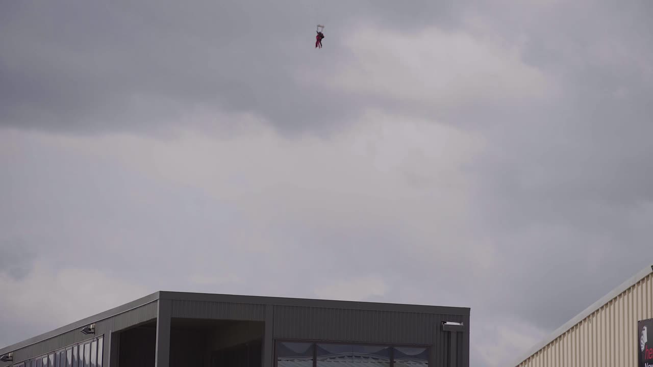 toma constante de un parapente naranja aterrizando sobre un edificio en wanaka