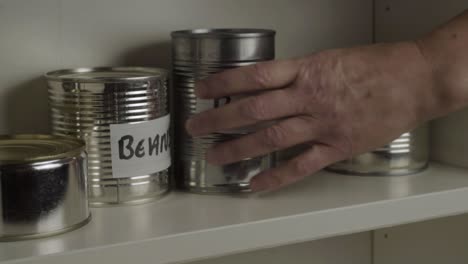 getting tins of aluminum baked beans out of food cupboard shelf