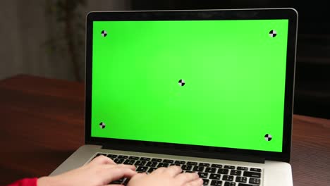 vista desde la parte de atrás niño sentado en la mesa escribiendo en la computadora portátil con tecla de croma verde