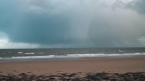 Timelapse-of-storm-rain-grey-clouds-raining-over-the-ocean-with-waves-crashing-onto-an-empty-beach-in-South-Shields,-England