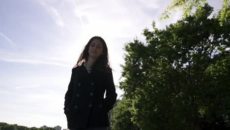 Retrato-De-Una-Bella-Y-Elegante-Modelo-Italiana-Caminando-En-Un-Parque-Tranquilo-Con-Un-Abrigo-Negro-En-Londres,-Reino-Unido