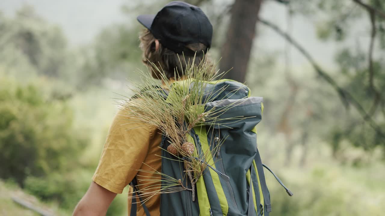Un hipster con uno zaino da turista cammina da solo tra le colline verdi.