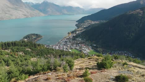 three young men travellers standing on queenstown hill track hike, new zealand and looking at the lake wakatipu, mountains with fresh snow and clouds - aerial drone