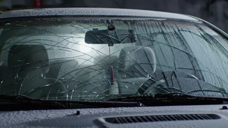 a close-up view of a car windshield exhibiting multiple cracks and water distortion, capturing the nature of damage and poor visibility