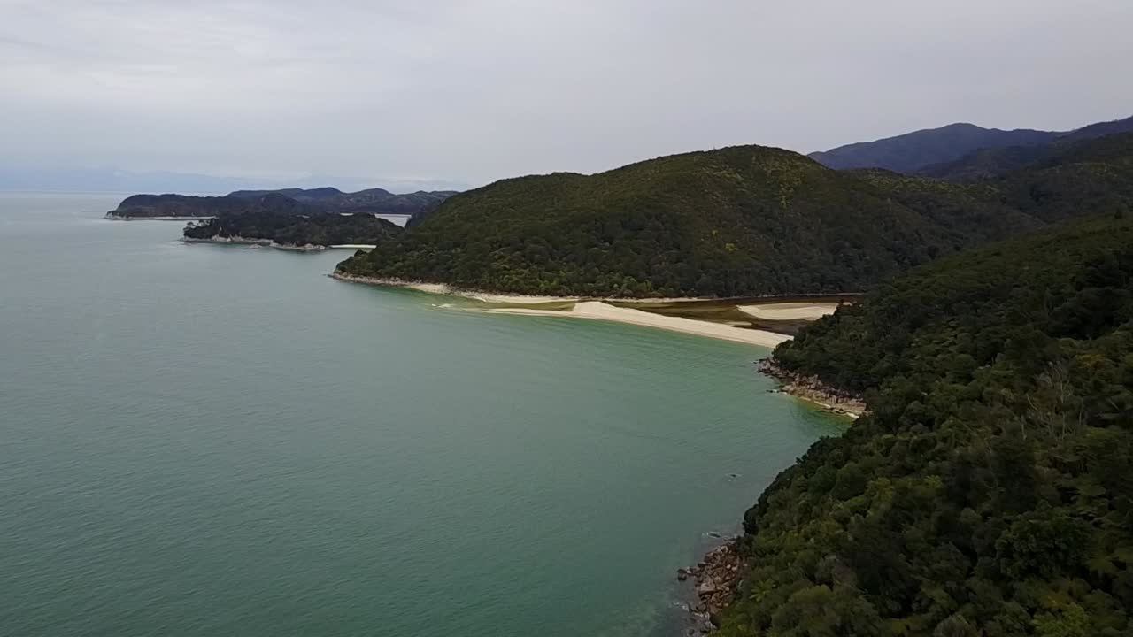 뉴질랜드 넬슨 아벨태즈먼 국립공원의 황금빛 모래 해변과 아름다운 녹색 산 위로 날아가는 공중 전망