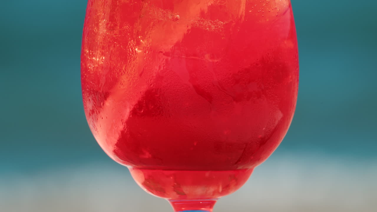 Close up of a refreshing red orange cocktail with orange slice and ice cubes, captured outdoors on a sunny day in Cannes