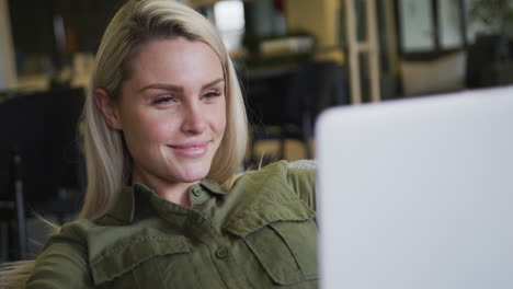 caucasian businesswoman sitting on pouf using a laptop in modern office