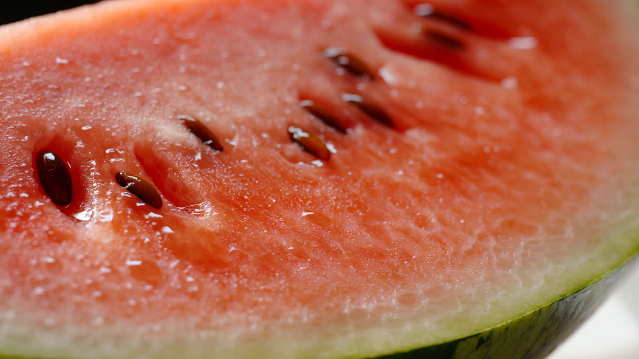 Primo Piano Semi di Fetta di Anguria Matura, Vista Macro di Polpa Scintillante e Semi Neri su Buccia Verde, Studio