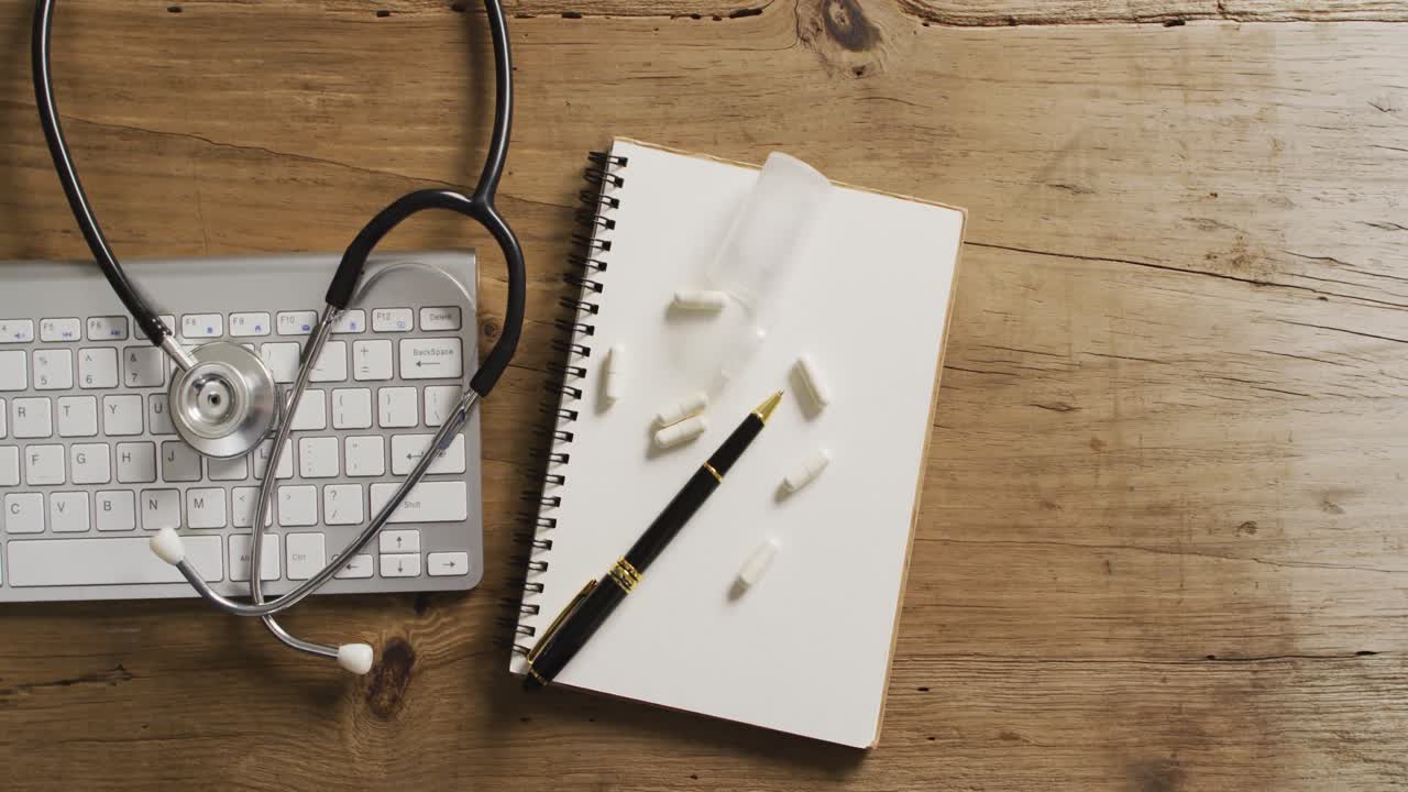 Video of close up of stethoscope with notebook and pills on wooden table