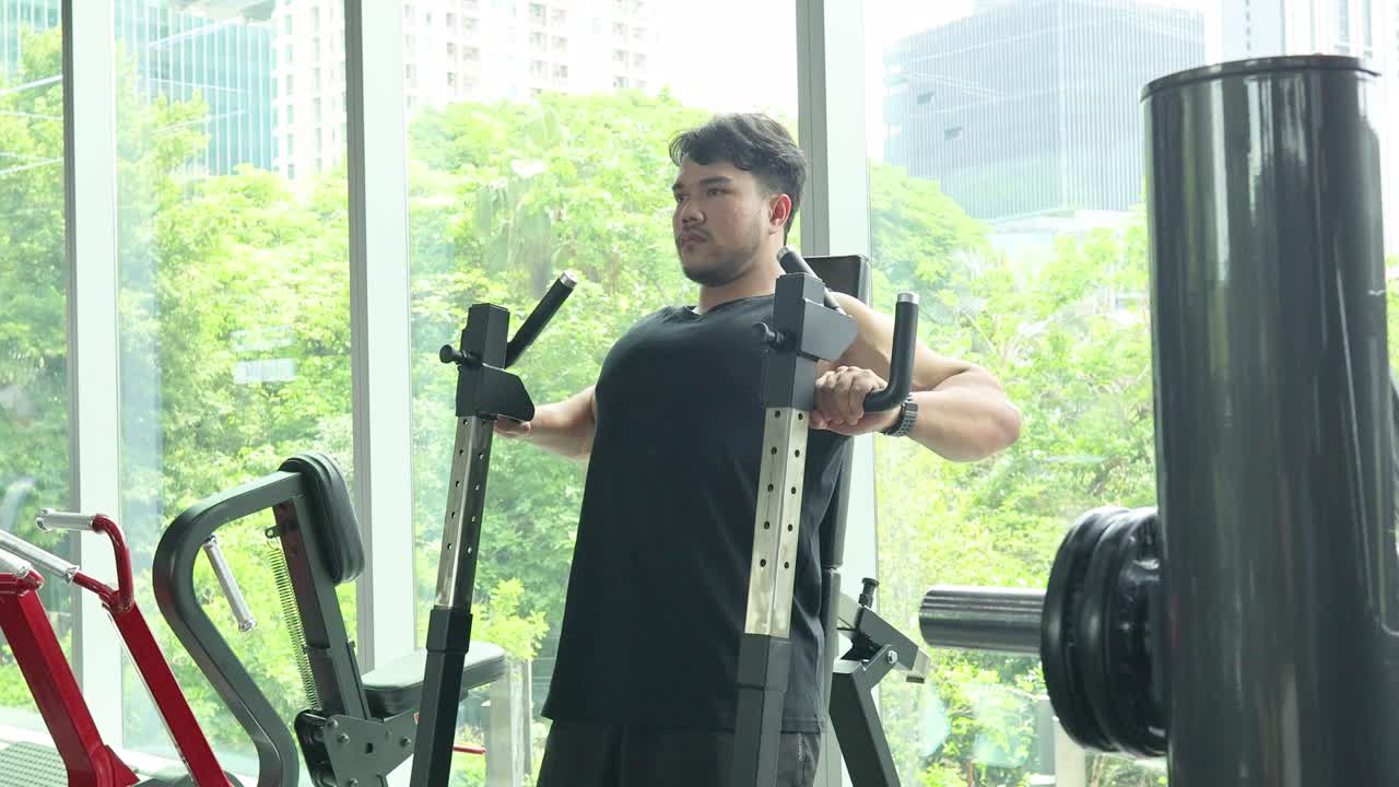A man performs chest press exercises in a well-lit gym with large windows