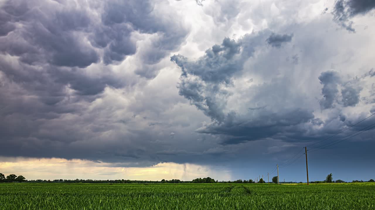 Dunkle Wolken bilden sich über einer ländlichen Gegend, in der Ferne ist der Regen als grauer Vorhang zu sehen