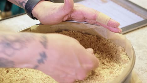 Tattooed female chef presses crumble crust into cheesecake spring pan