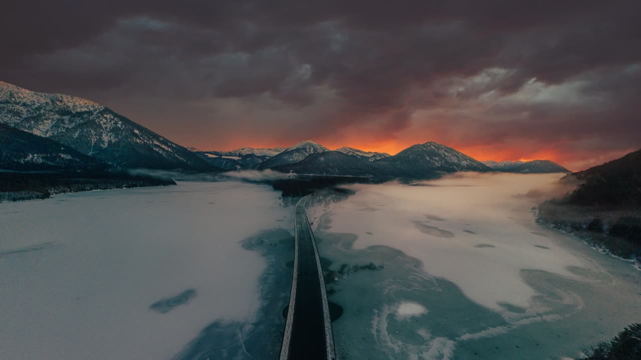 cinemagraph aerial seamless video loop time lapse de sylvenstein sylvensteinspeicher presa, un pintoresco e idílico valle de lago de montaña en invierno con hielo y nieve en los alpes austriacos bávaros con cordilleras y picos en el atardecer rojo vibrante y nubes.