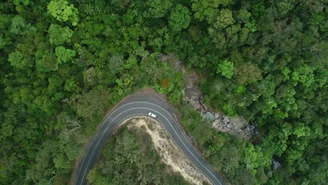 vista aérea de un automóvil que conduce en un camino estrecho en medio de una selva tropical con una cascada cercana y un arroyo que fluye con agua