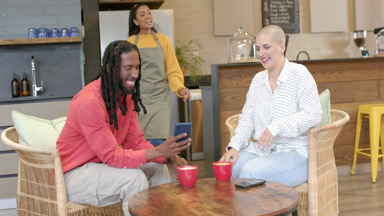 Diverse friends laughing and sharing phone at coffee shop leading server walking examining screen
