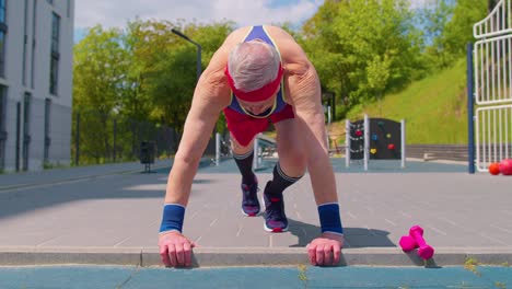 senior man grandfather 80 years old doing sport cardio training push-ups exercising on playground