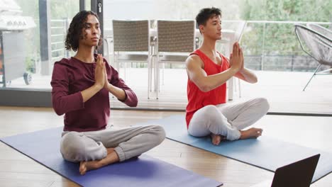 happy diverse male couple doing yoga, meditating in living room
