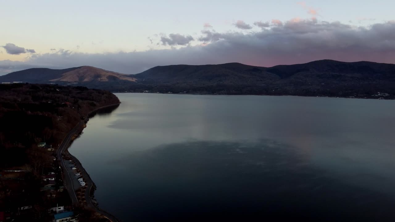 Twilight hues over a tranquil lake with mountain backdrop, aerial view