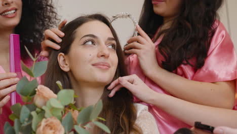 close-up vista do grupo de amigas que compõem a noiva e colocando-lhe uma faixa de cabelo enquanto segura um buquê sentado na cama na reunião nupcial