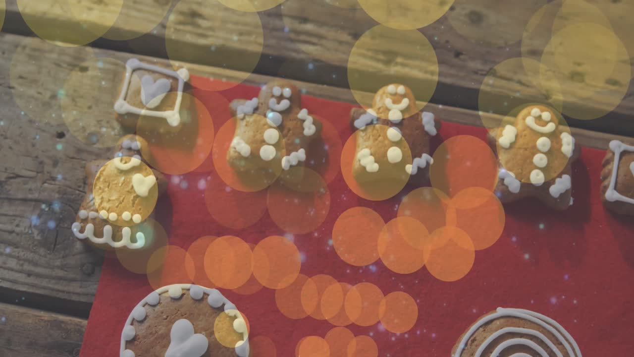 Animation of yellow and orange light spots over christmas gingerbread men and decorated cookies