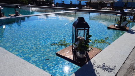 luxury pool decor. a romantic lantern candle and a vase of flowers float on the water's surface on a sunny day.