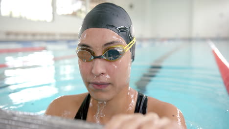 female swimmer in goggles and swim cap resting at edge of indoor pool