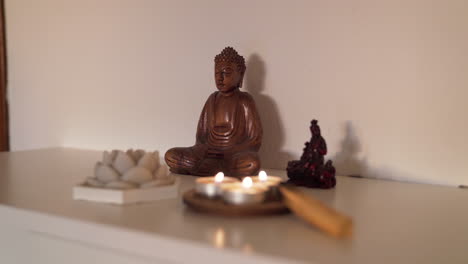 Hölzerne-Buddha-Gottesfigur-Auf-Einem-Hausaltar-Neben-Einigen-Kerzen-Und-Palo-Santo-Mit-Sonnenuntergangsbeleuchtung