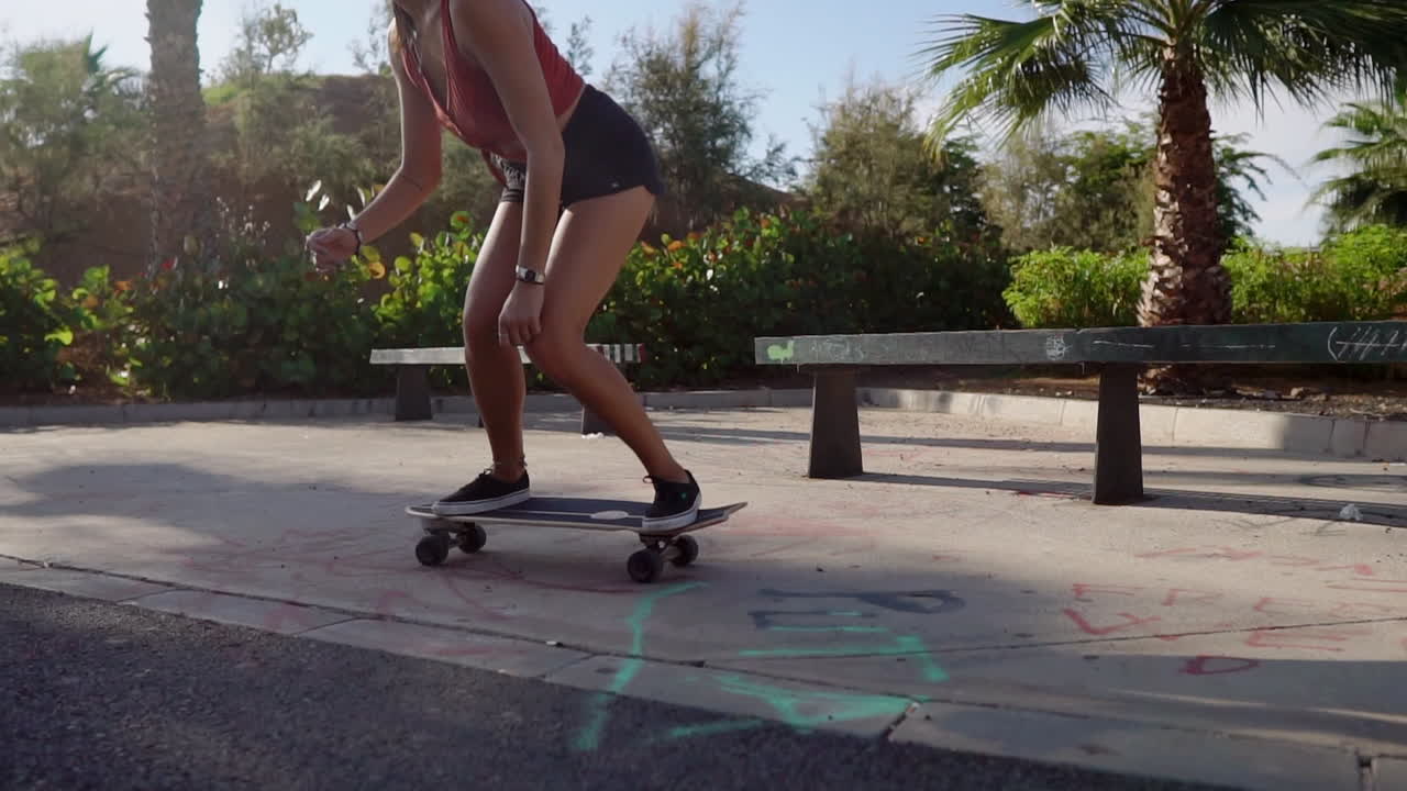 ⁇ 나무 사이 에서, 슬로우 모션 은 아름다운 젊은 소녀 가 해변 에 인접 한 도로 에서 롱보드 를 부드럽게 타고 있는 것 을 보여 준다
