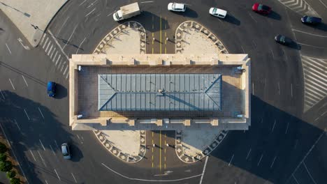 Vista-Aérea-De-Arriba-Hacia-Abajo-Sobre-El-Arco-Del-Triunfo-En-Bucarest,-Rumania,-Con-Automóviles-Circulando-En-La-Rotonda.