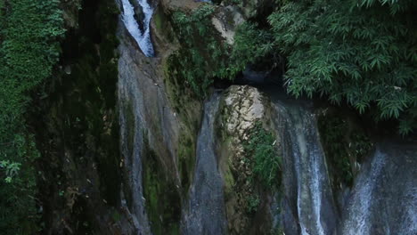 small stream of water flowing down the base of kempty waterfalls in mussorie, india, tilt down slow motion shot.
