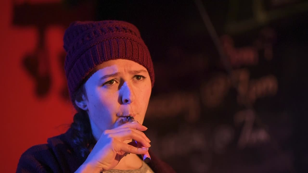 молодая женщина серьезно говорит на сцене и курит vape pen, прежде чем уйти вправо