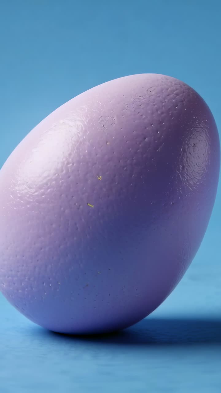 Vertical video: Tilting purple egg rolling right on blue tabletop, reacting to small push, settling