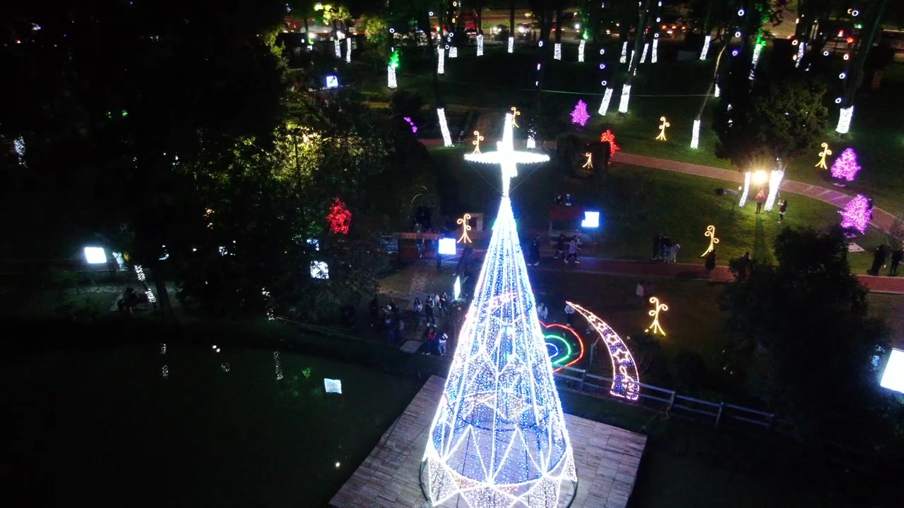 Gran árbol de Navidad iluminado por una brillante estrella en la cima, rodeado de múltiples luces en el Parque de los Novios, Bogotá. Toma panorámica con dron