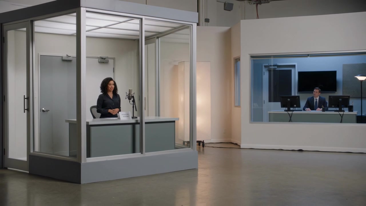 Ao sinal, apresentador(a) de blusa preta falando ao microfone em uma cabine de gravação, produtor sinalizando, espaço para texto