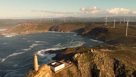 Aerial-view-of-lighthouse-top-of-ocean-rock-cliff-with-windmill-turbine-farm-land