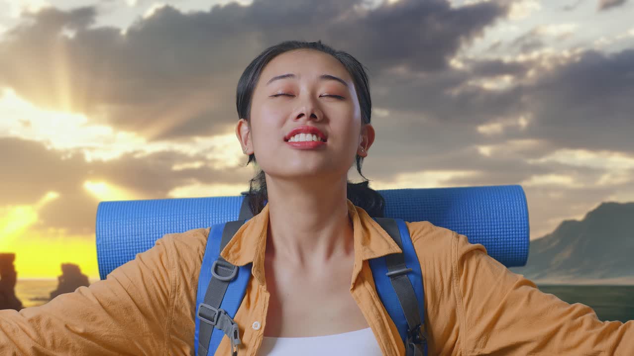Close Up Of Asian Female Hiker With Mountaineering Backpack Smiling And Spreading Arms Enjoy Looking The View Around While Standing on Beach During Sunset Time
