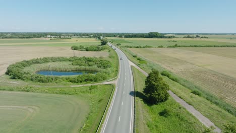 aerial establishing shot of a rural landscape, countryside road with trucks and cars moving, lush green agricultural crop fields, sunny summer day, wide drone shot moving forward