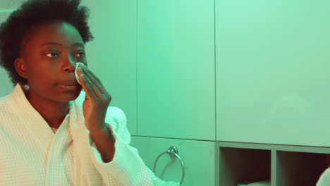 african american woman applying lotion to face in bathroom