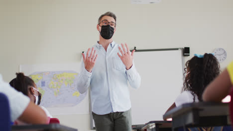 caucasian male teacher wearing face mask teaching students in the class at school