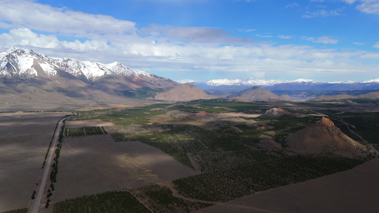 아르헨티나의 안데스 산맥에 있는 루트 40의 드론 파노라마 전망: 휘어지는 도로가 경계를 가로지르고, 언덕 사이에는 광활한 농경지가 있고, 구름의 그림자가 풍경을 고 있다.